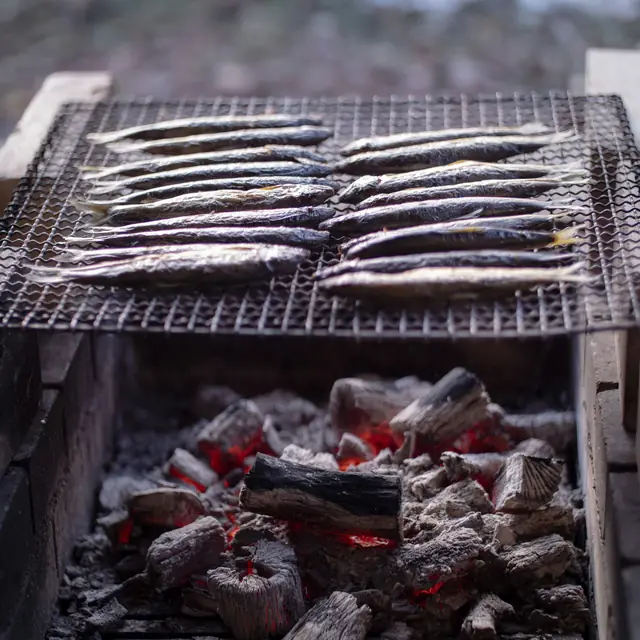 Sardines grilling over charcoal.